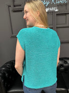 Woman wearing a teal sleeveless top standing in front of a black leather couch.