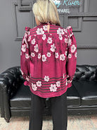 Person wearing a pink floral jacket sitting on a black leather couch.
