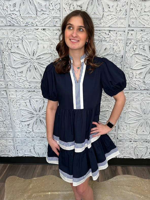 Woman wearing a navy dress with white trim against a decorative tiled wall.