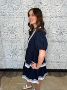 Woman wearing a navy dress with white trim against a decorative tiled wall.