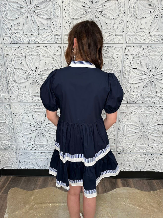 Person wearing a navy dress with white trim against a decorative tiled wall.