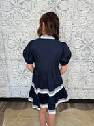 Person wearing a navy dress with white trim against a decorative tiled wall.