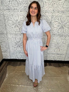 Woman in a white and blue striped dress standing against a decorative tiled wall.