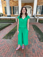 Woman in a green jumpsuit standing on a brick path in front of a building.