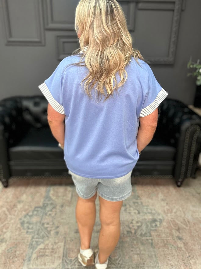 Person wearing a light blue t-shirt with white trim and denim shorts in a room.