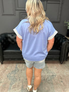 Person wearing a light blue t-shirt with white trim and denim shorts in a room.