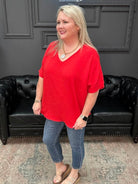 Woman in a red shirt and blue jeans standing in front of a black leather couch.