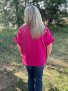 Person wearing a pink shirt and blue jeans standing in a natural setting with trees and grass.