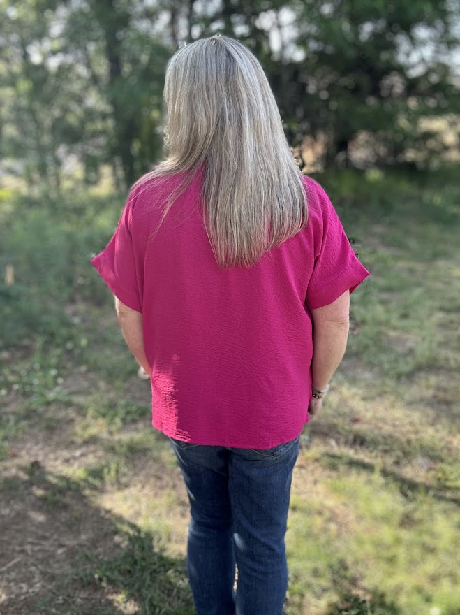 Person wearing a pink shirt and blue jeans standing in a natural setting with trees and grass.