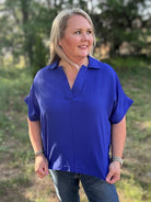 Woman wearing a blue shirt standing outdoors with greenery in the background