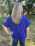 Person wearing a blue shirt standing in a grassy outdoor area with trees in the background