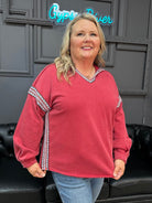 Woman wearing a red sweater with decorative sleeves in a room with a gray wall and black leather couch.