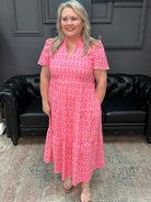 Woman in a pink dress standing in a room with a black leather couch and gray walls.