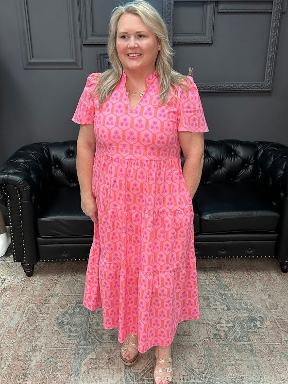 Woman in a pink dress standing in a room with a black leather couch and gray walls.
