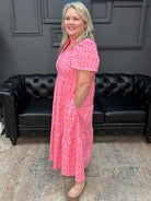 Woman in a pink dress standing in a room with a black leather couch and gray walls.