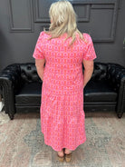 Woman wearing a pink dress standing in a room with a black leather couch.