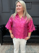 Woman wearing a pink blouse and white pants standing in a room with a black leather couch and gray walls.