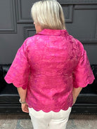Woman wearing a pink textured blouse and white pants in a store setting.