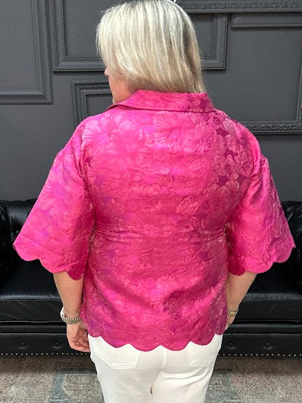 Woman wearing a pink textured blouse and white pants in a store setting.