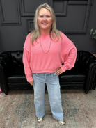 Woman wearing a pink sweater and blue jeans standing in a room with dark walls and a black leather couch.