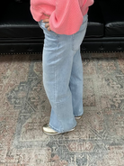 Woman in a pink sweater and blue jeans standing in a room with a black leather sofa and decorative items.