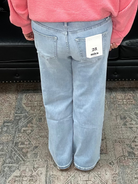 Person wearing a pink sweater and light blue jeans standing in a room with a black leather sofa and patterned rug.