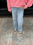 Woman wearing a pink sweater and blue jeans standing in a room with a black leather couch and floral rug.