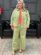Woman in a green outfit standing in a room with a black leather couch and a neon sign.