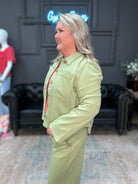 Woman wearing a light green jacket and pants in an indoor setting with a decorative wall and furniture.