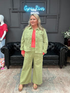 Woman in a green outfit standing in front of a black couch with 'Gypsy River Apparel' sign.