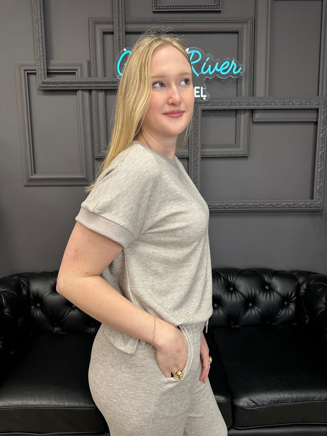 Woman in a gray outfit standing in front of a black leather couch with a decorative wall in the background.