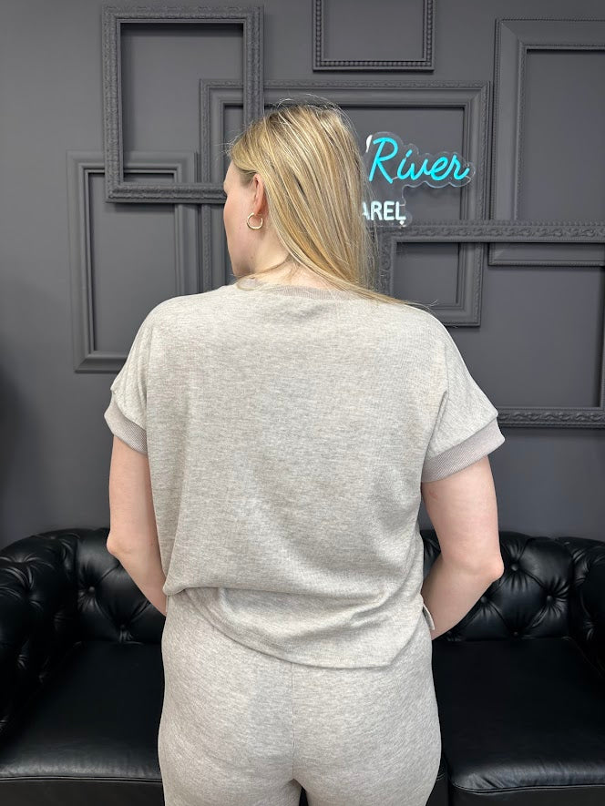 Person wearing a gray outfit standing in front of a dark wall with framed pictures and a neon sign.