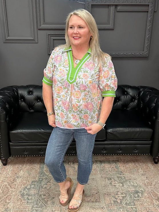 Woman wearing a floral shirt with green trim standing in front of a black leather couch.