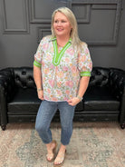 Woman wearing a floral shirt with green trim standing in front of a black leather couch.