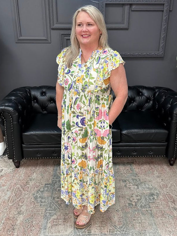 Woman in a floral dress standing in front of a black leather couch and gray wall.
