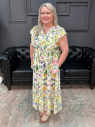 Woman in a floral dress standing in front of a black leather couch and gray wall.