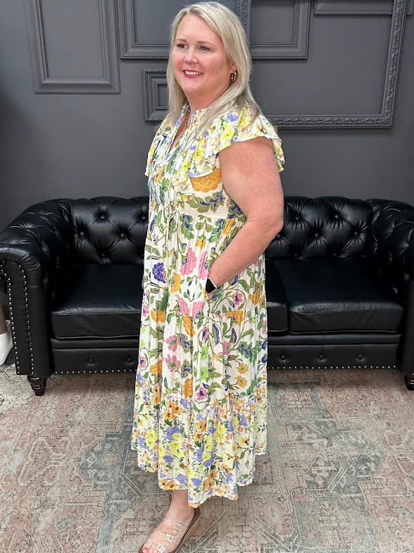 Woman in a floral dress standing in a room with black leather couches and a gray wall.
