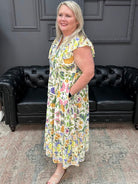 Woman in a floral dress standing in a room with black leather couches and a gray wall.