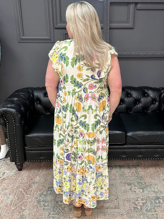 Woman in a floral dress standing in front of a black leather couch with a gray wall and 'Apparel' sign in the background.