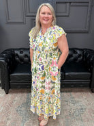 Woman in a floral dress standing in front of black leather chairs with a dark gray wall and neon sign in the background.