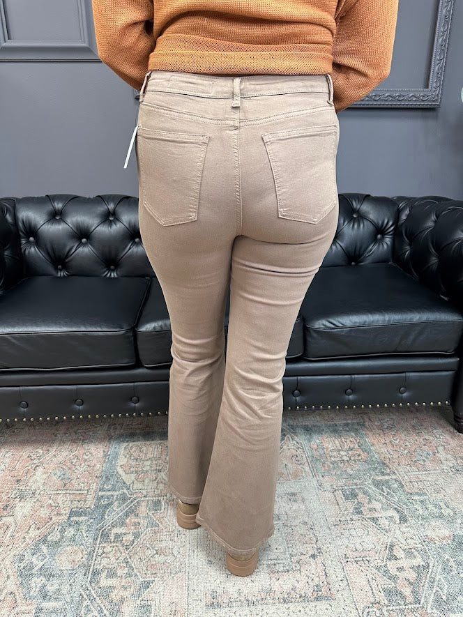 Person wearing beige pants standing in a room with a black leather couch and gray wall.