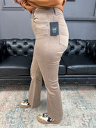 Person wearing beige pants with a brand tag in a room with a black leather couch.