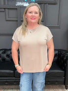Woman wearing a beige t-shirt and blue jeans standing in front of a black leather couch.
