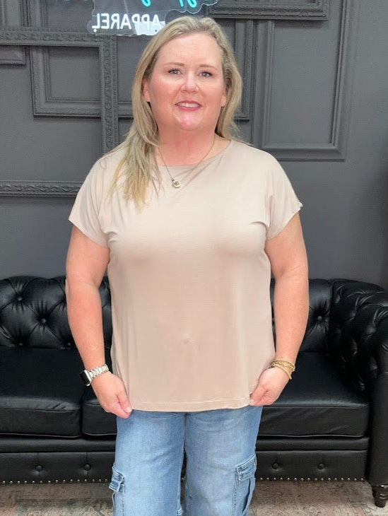 Woman wearing a beige t-shirt and blue jeans standing in front of a black leather couch.