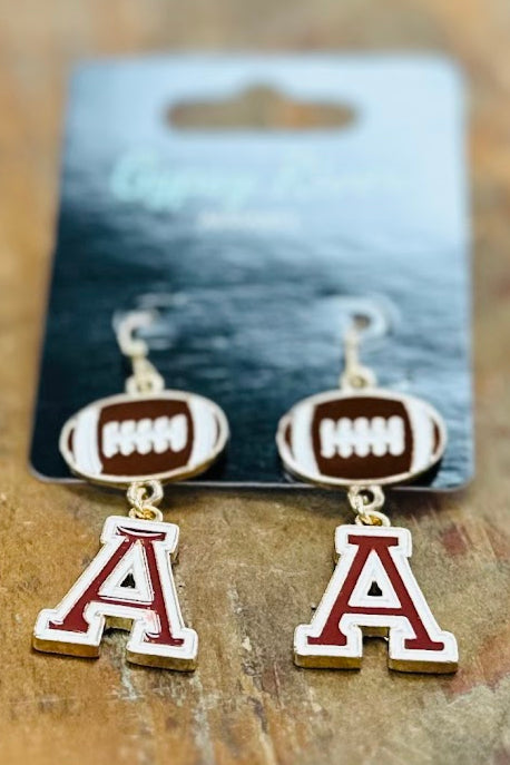 Pair of earrings with 'A' and football design on a card, placed on a wooden surface. Gameday. Crimson Tide.