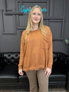 Person wearing a brown sweater standing in front of a black couch with a neon sign in the background.