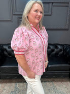 Woman wearing a pink blouse with white pants in a room with a black leather couch and gray walls.