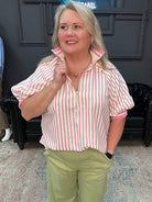 Woman in a striped shirt and green pants standing in a room with a neon sign and mannequin.