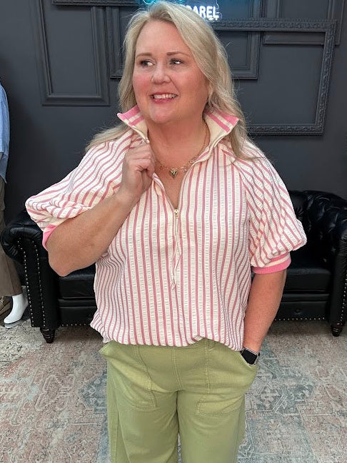 Woman in a striped shirt and green pants standing in a room with a neon sign and mannequin.