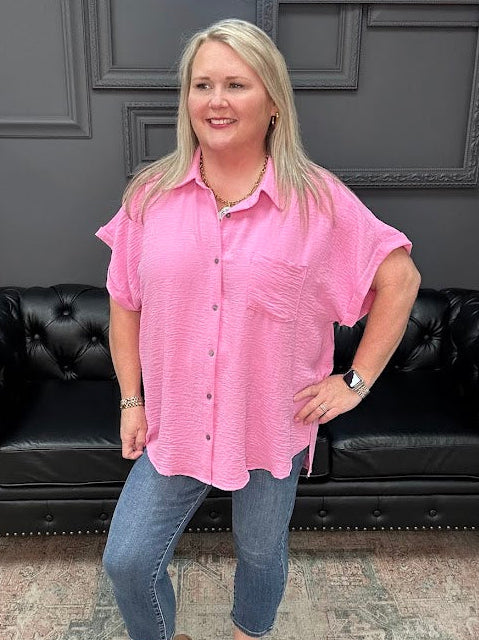 Woman wearing a pink shirt and blue jeans standing in front of a black leather couch.